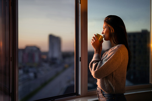 Woman thinking about her hysterectomy options as she looks out the window drinking coffee