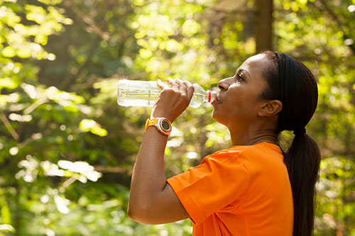 woman drinking water while exercising in the woods