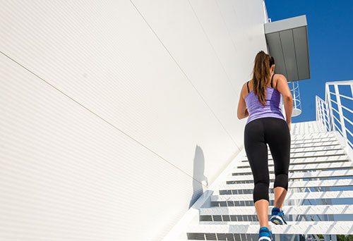 A female athlete running up a set of stairs outside to relieve her early menopause symptoms and support bone health. female athlete running up stairs outside to relieve early menopause