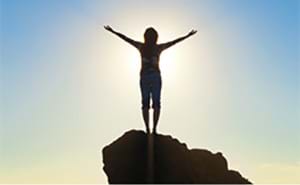 A silhouette of a woman with her hands up in the air on a rock letting go of her anger. silhouette of woman with hands in air on a rock