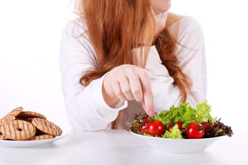 Woman enjoys eating healthy so she chooses salad vegetables instead of cookies. woman choosing salad vegetables instead of cookies