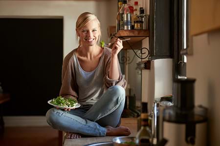 woman sitting on counter at home eating a healthy salad