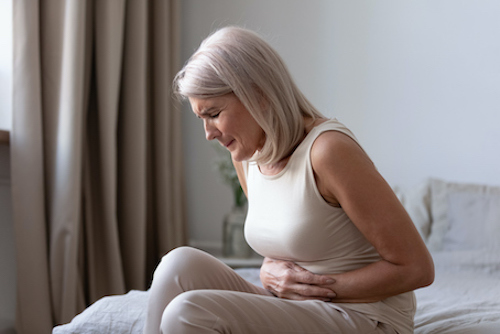 A woman sitting on her bed holding her stomach in pain with digestive issues. 