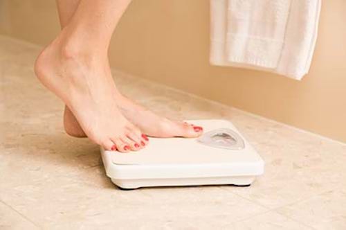 Woman standing on a scale to monitor her weight for bone health. 